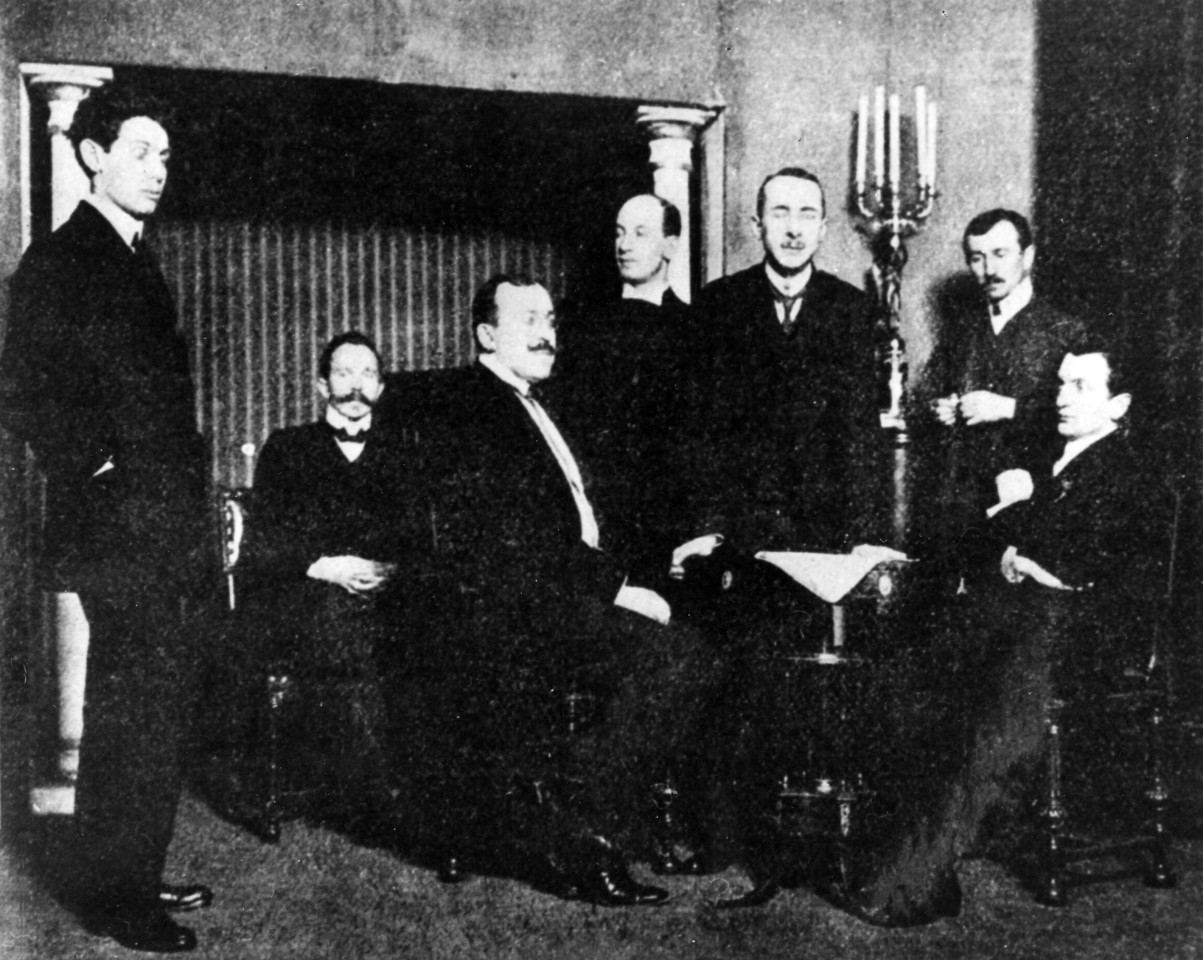 Siedmiu mężczyzn pozujących do zdjęcia. Część z nich siedzi, część stoi.