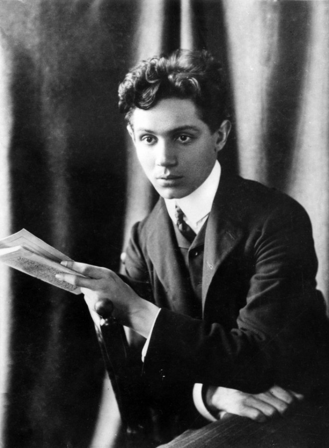 Czarno białe zdjęcie z portretem młodego mężczyzny trzymającego kilka kartek w dłoni.