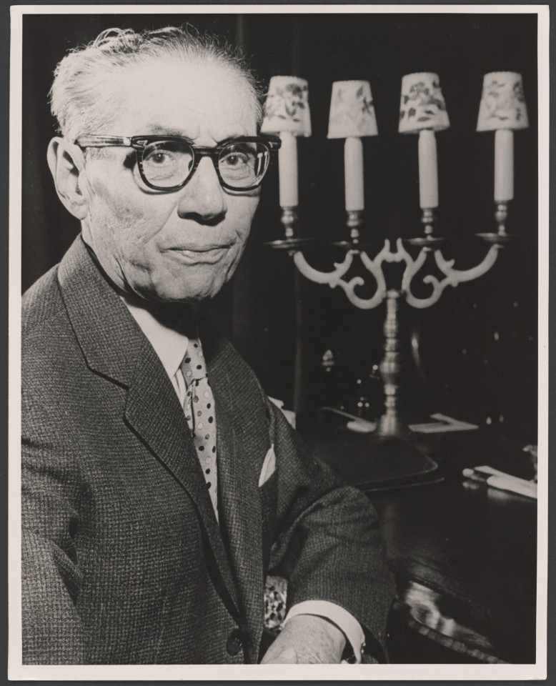 Na czarno-białym zdjęciu Arnold Szyfman w swoim domu przy ulicy Prezydenckiej. Starszy mężczyzna w okularach ze świecznikiem.