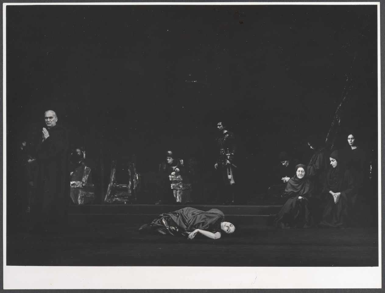 Na czarno-białym zdjęciu grupa aktorów na scenie pośród scenografii teatralnej spektaklu Irydion.