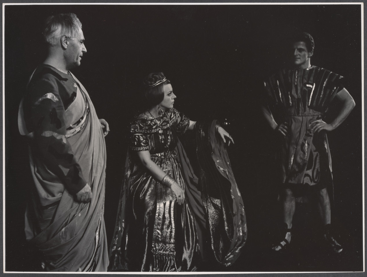 Na czarno-białym zdjęciu grupa aktorów na scenie w rolach podczas spektaklu Irydion.
